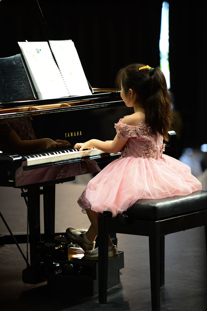 Young piano performer, sitting at piano playing on stage, wearing a pink dress